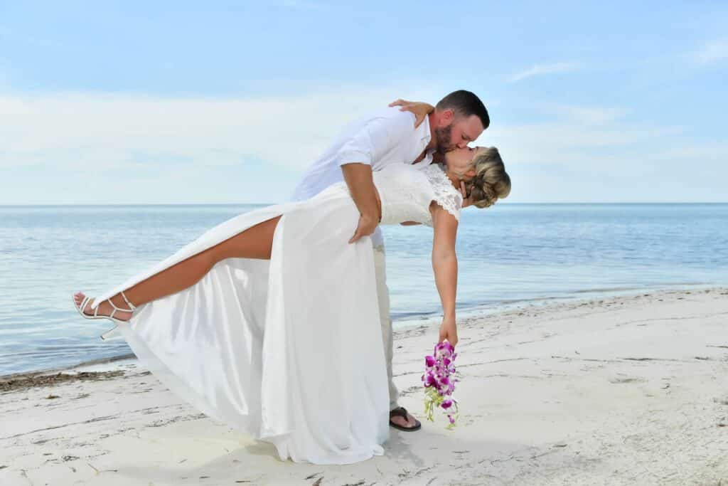 Couple sharing a romantic kiss during their vow renewal on the beach at Sandals South Coast in Jamaica.