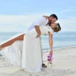 Couple sharing a romantic kiss during their vow renewal on the beach at Sandals South Coast in Jamaica.