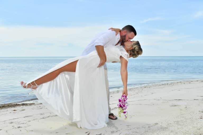 Couple sharing a romantic kiss during their vow renewal on the beach at Sandals South Coast in Jamaica.