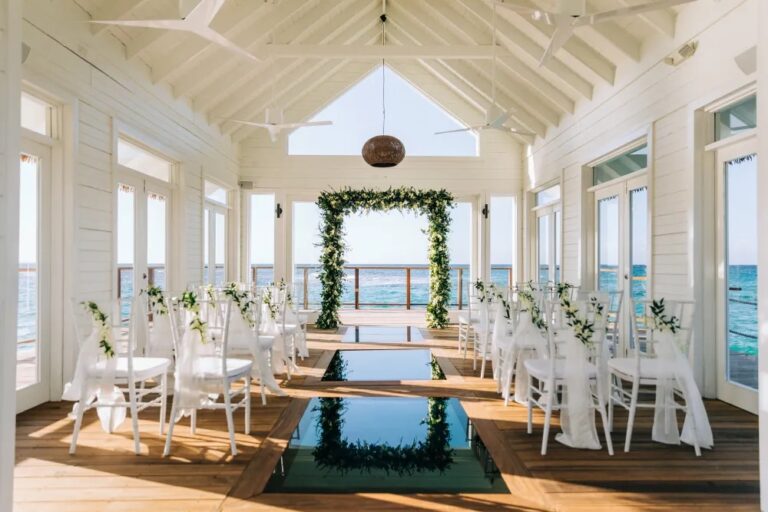 An elegant overwater wedding chapel at Sandals Resorts in Jamaica, featuring white chairs, floral decorations, and panoramic ocean views.