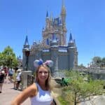 Guest smiling in blue skirt on side of Cinderella Castle at Magic Kingdom