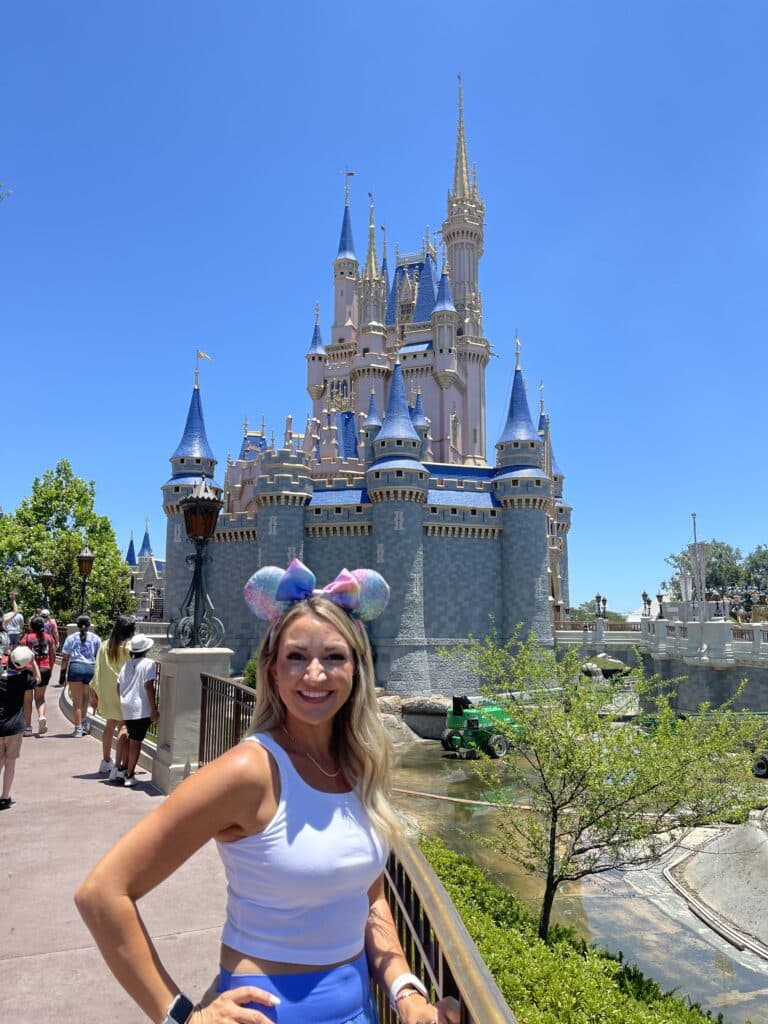 Guest smiling in blue skirt on side of Cinderella Castle at Magic Kingdom