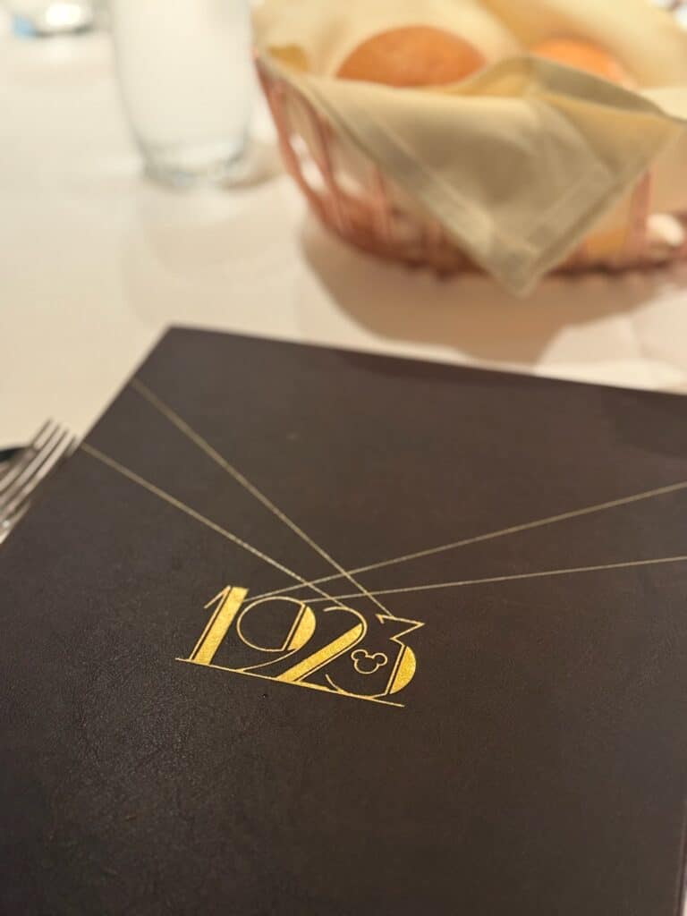 Elegant Disney Cruise Line dining experience at 1923 restaurant, featuring the menu with golden lettering and fresh bread on the table.