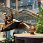 The grand atrium of the Disney Treasure cruise ship featuring the Aladdin and Jasmine statue with a golden magic lamp in the foreground.