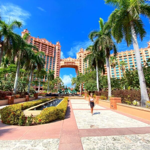 Walking toward the Atlantis Royal Towers on Paradise Island, Bahamas Woman walking along the beautifully landscaped path in front of the iconic Atlantis Royal Towers on Paradise Island in the Bahamas, surrounded by palm trees under a bright blue sky.