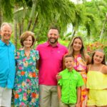 Smiling family of six posing together among lush palms and tropical flowers at Beaches Turks & Caicos, dressed in bright colorful outfits during a Caribbean family vacation.