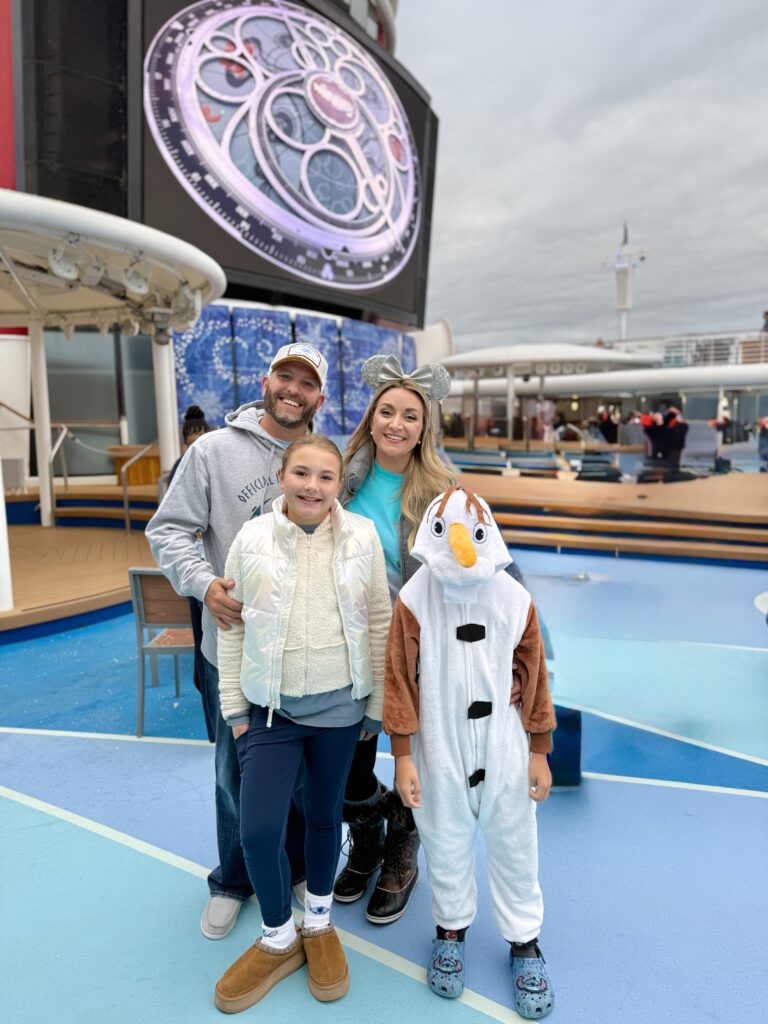 Family on the top deck of the Disney Wonder during the Frozen deck show in Alaska, with their son dressed as Olaf and the ship’s giant screen in the background.