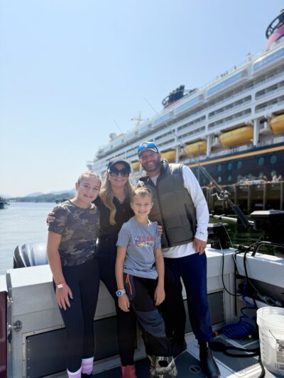 Family posing on a fishing boat in Ketchikan, Alaska, during a Disney Alaska Cruise port excursion for king salmon fishing, with the Disney Wonder docked in the background.