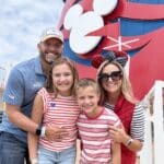 Family of four smiling on the top deck of the Disney Wonder in front of the ship’s iconic red smokestack with the Mickey Mouse logo.