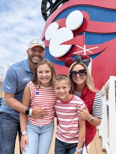Family of four smiling on the top deck of the Disney Wonder in front of the ship’s iconic red smokestack with the Mickey Mouse logo.