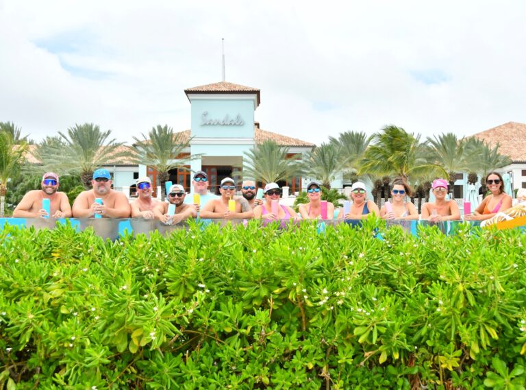 Group of friends from Traveling Ears Vacations’ annual trip relaxing together in the infinity pool at Sandals resort in Curaçao.