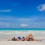 Woman relaxing on the soft white sands of Disney’s Lookout Cay at Lighthouse Point with turquoise water and blue skies in the background.