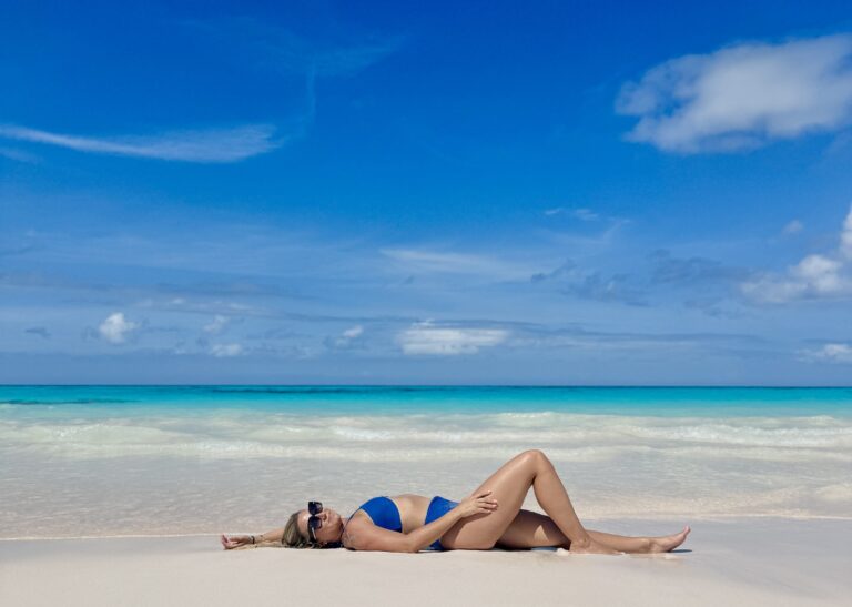 Woman relaxing on the soft white sands of Disney’s Lookout Cay at Lighthouse Point with turquoise water and blue skies in the background.