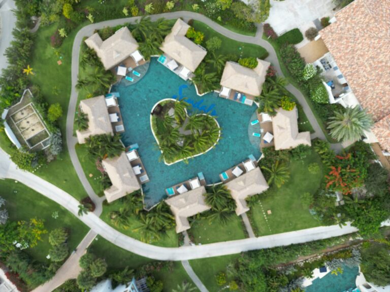 Woman in a colorful swimsuit smiling under a palm tree at Sandals Royal Curaçao on a sunny Caribbean day.