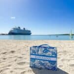 Castaway Cay beach bag on the sand with the Disney Fantasy cruise ship anchored in the turquoise waters of Disney’s private island.