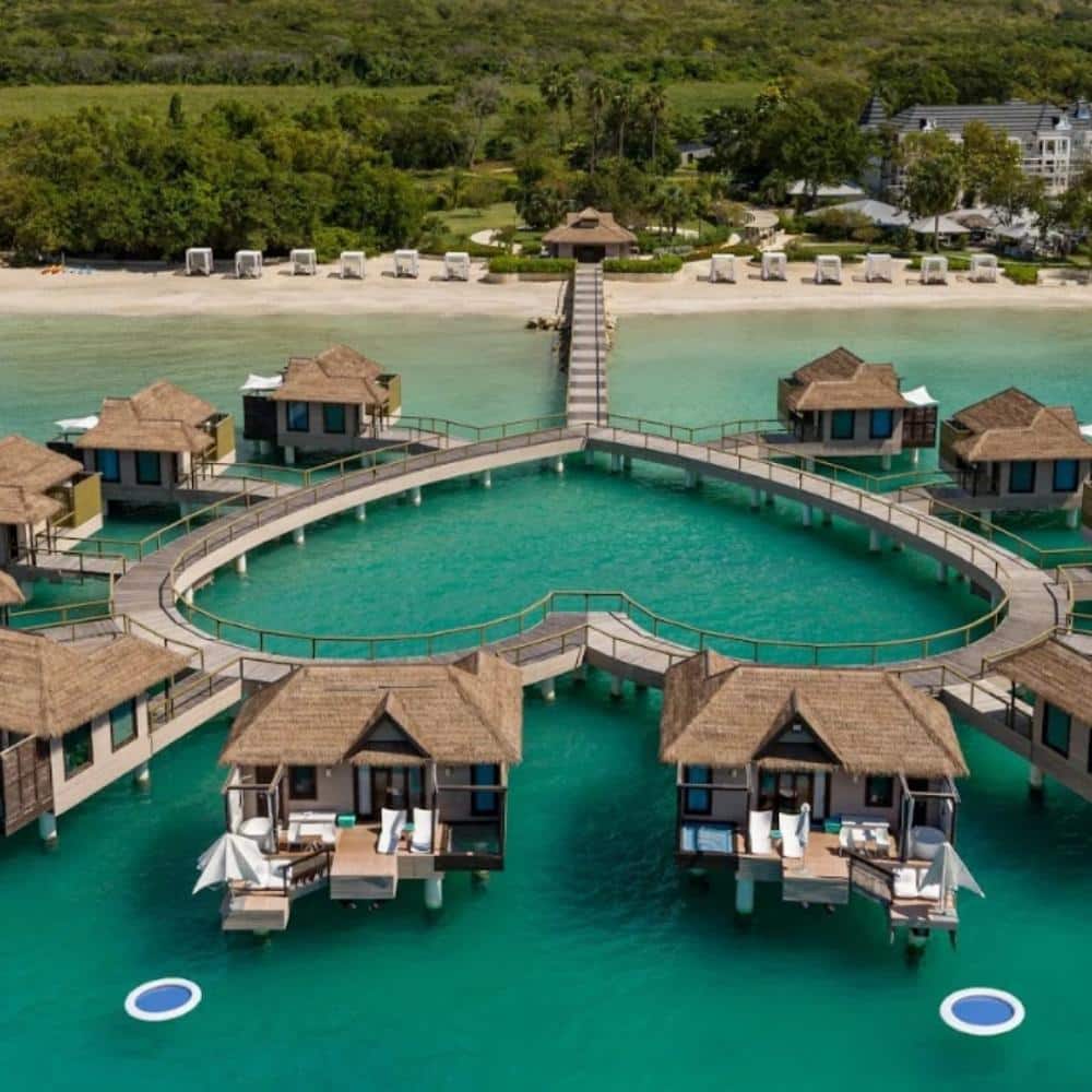 Overwater bungalows at a Sandals resort in the Caribbean with clear blue water.