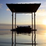 Open-air daybed pavilion reflected in water at sunset at Amanyara in Turks and Caicos