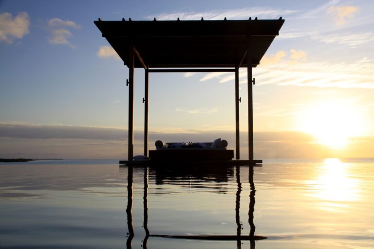 Open-air daybed pavilion reflected in water at sunset at Amanyara in Turks and Caicos