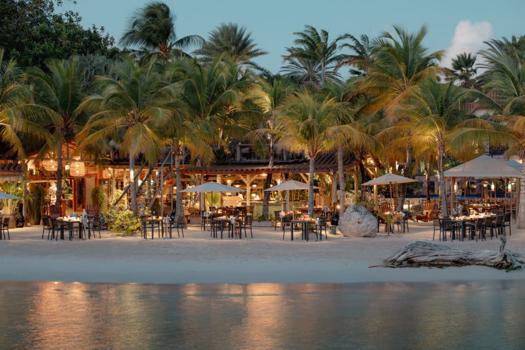 Palm-lined beachfront and resort dining area at Baoase Luxury Resort in Curaçao beside calm Caribbean water
