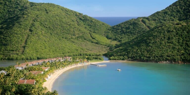 Aerial view of Carlisle Bay Antigua resort along a sheltered beach between lush green hills and blue Caribbean water