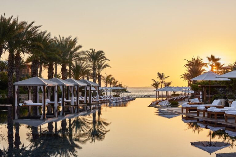 Sunset over the reflective resort pool, cabanas and palm trees at Chileno Bay Resort in Los Cabos, Mexico