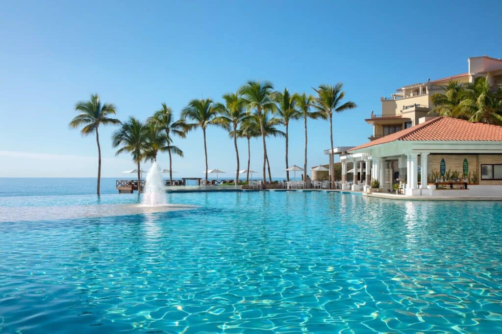 Oceanfront pool with palm trees and resort buildings at Dreams Los Cabos in Mexico