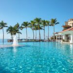 Oceanfront pool with palm trees and resort buildings at Dreams Los Cabos in Mexico