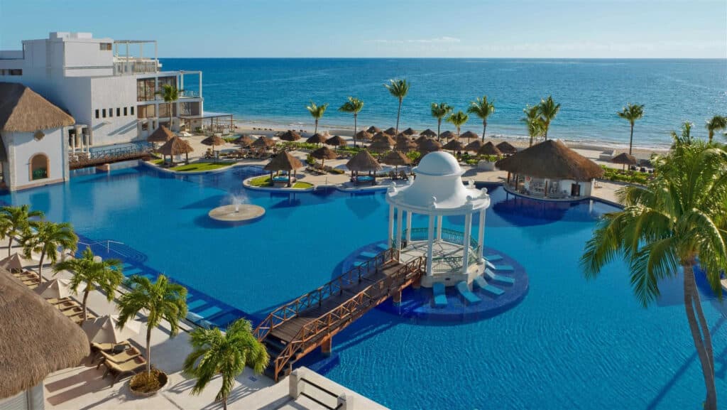 Elevated view of the main pool, palm trees and Caribbean beachfront at Dreams Sapphire Resort & Spa in Puerto Morelos, Mexico