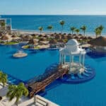 Elevated view of the main pool, palm trees and Caribbean beachfront at Dreams Sapphire Resort & Spa in Puerto Morelos, Mexico