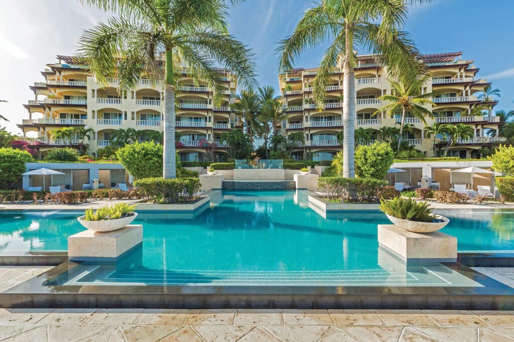 Turquoise resort pool framed by palms and luxury guest buildings at Grace Bay Club in Turks and Caicos