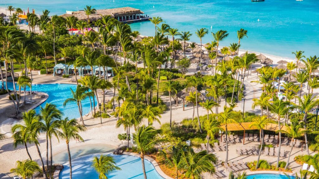Elevated view of the pools, palm trees and turquoise beachfront at Hilton Aruba Caribbean Resort