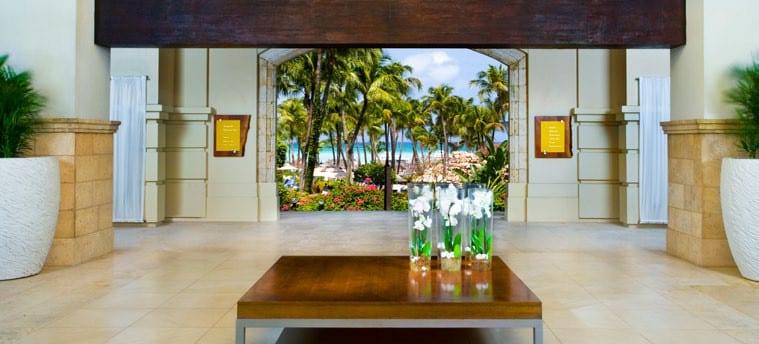 Open-air lobby at Hyatt Regency Aruba framing palm trees and tropical resort grounds toward Palm Beach