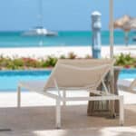 White loungers beside the pool with Palm Beach and turquoise Caribbean water at Hyatt Regency Aruba
