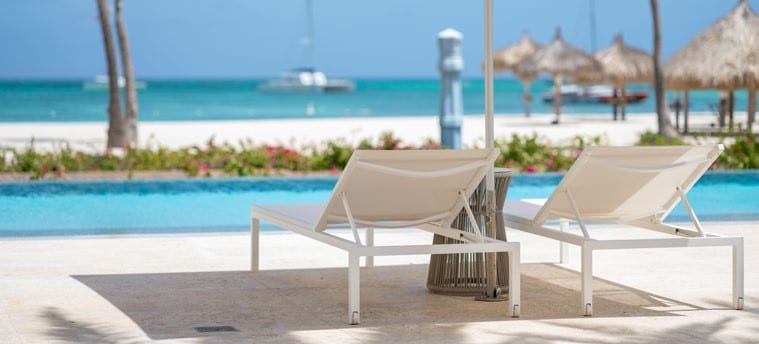 White loungers beside the pool with Palm Beach and turquoise Caribbean water at Hyatt Regency Aruba