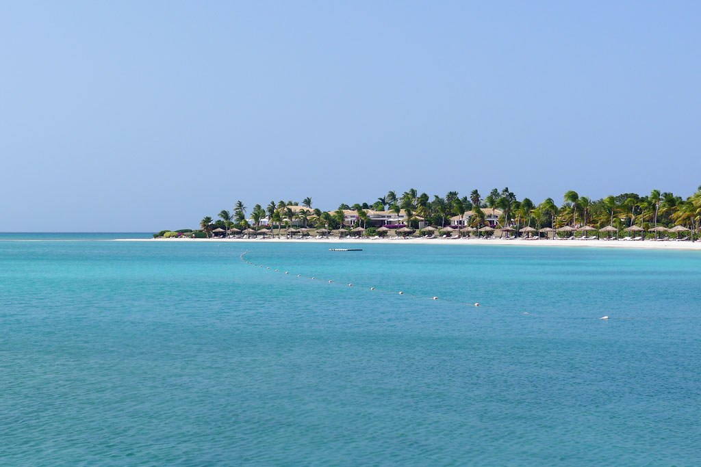 Jumby Bay Island resort buildings and palms viewed across vivid turquoise Caribbean water in Antigua