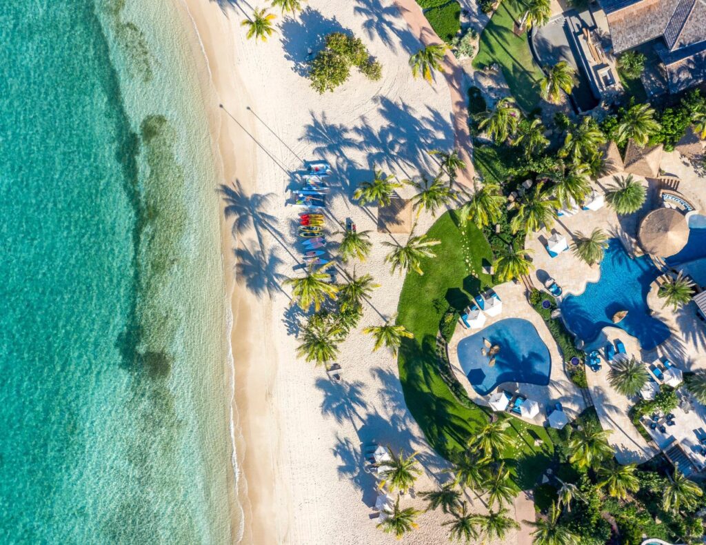 Aerial view of Oil Nut Bay Beach Club pools, palm trees and white sand beside turquoise water on Virgin Gorda