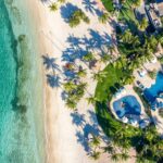 Aerial view of Oil Nut Bay Beach Club pools, palm trees and white sand beside turquoise water on Virgin Gorda