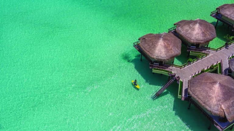 Aerial view of Palafitos Overwater Bungalows above turquoise water at El Dorado Maroma in Riviera Maya