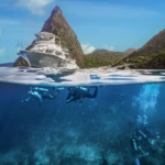 Scuba divers in Saint Lucia beneath a Sandals dive boat with the Pitons in the background