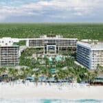 Beachfront view of Secrets Moxché Playa del Carmen with the resort buildings, pools, white sand and Caribbean Sea
