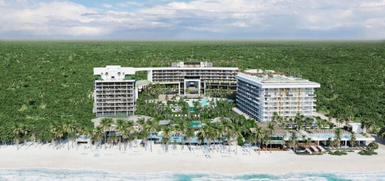 Beachfront view of Secrets Moxché Playa del Carmen with the resort buildings, pools, white sand and Caribbean Sea