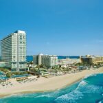 Aerial view of the Secrets The Vine Cancun tower, pools and white-sand beach along the Caribbean Sea