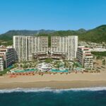 Aerial view of Secrets Vallarta Bay with its beachfront tower, pools and mountains in Puerto Vallarta