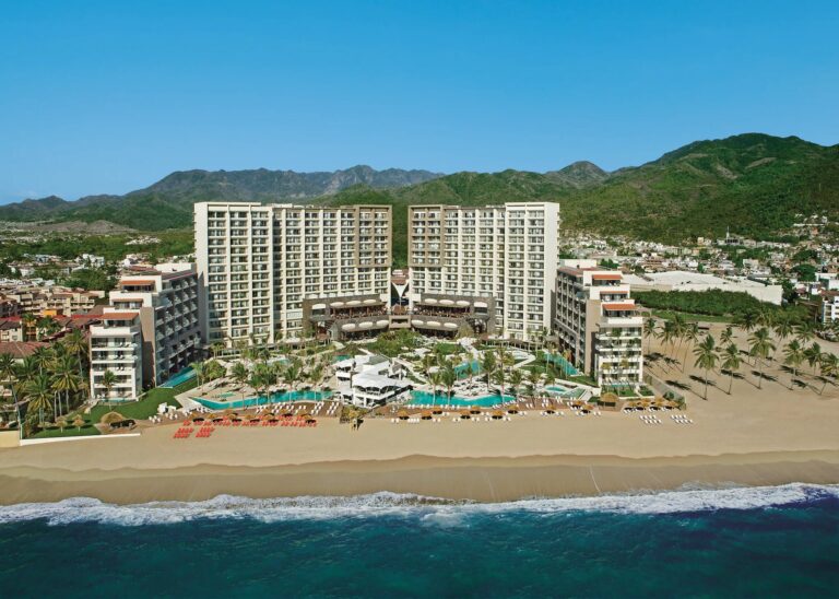 Aerial view of Secrets Vallarta Bay with its beachfront tower, pools and mountains in Puerto Vallarta