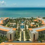 Aerial view of UNICO 20°87° Riviera Maya with curved resort buildings, pools, palms and the Caribbean Sea