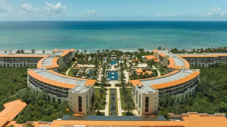 Aerial view of UNICO 20°87° Riviera Maya with curved resort buildings, pools, palms and the Caribbean Sea