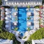 Top-down view of the large blue pool, white resort buildings and palms at Wymara Resort in Turks and Caicos