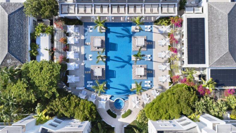 Top-down view of the large blue pool, white resort buildings and palms at Wymara Resort in Turks and Caicos