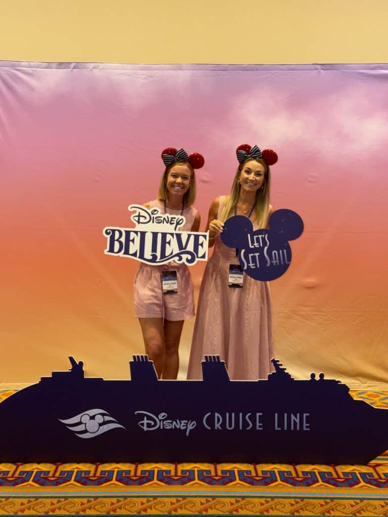 Two attendees holding Disney Believe and Let's Set Sail signs at the reveal event
