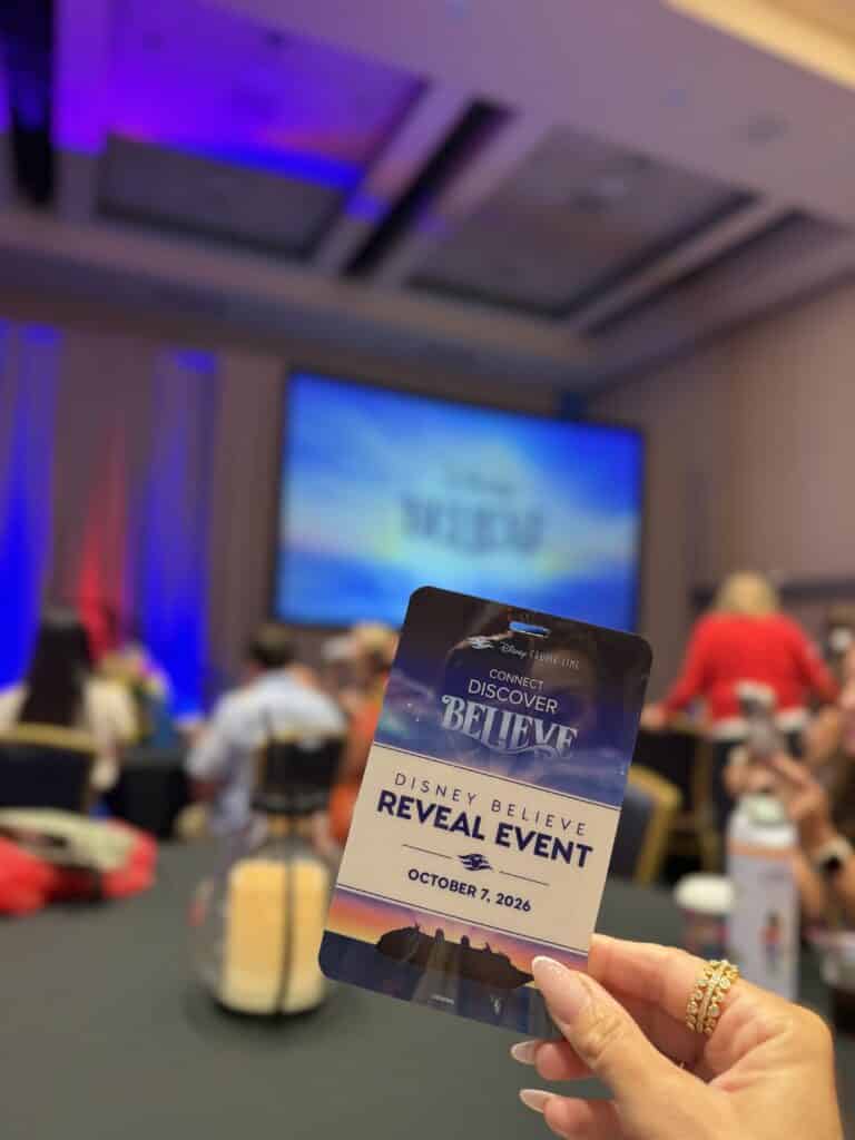 Disney Believe reveal event badge dated October 7, 2026, held in front of the presentation screen